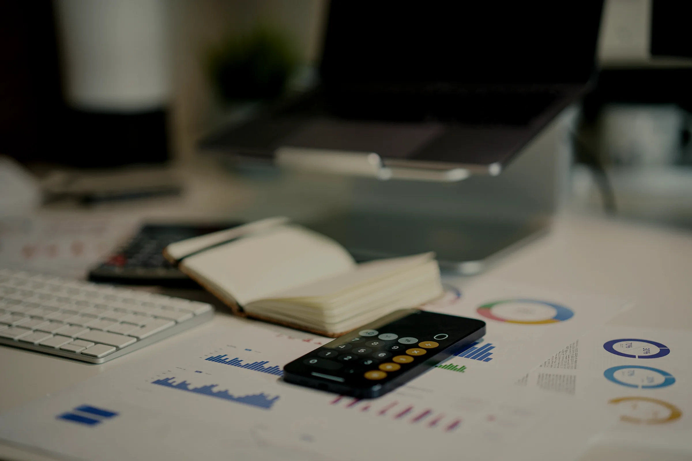 An open notebook, calculator and printed figures on a desk.